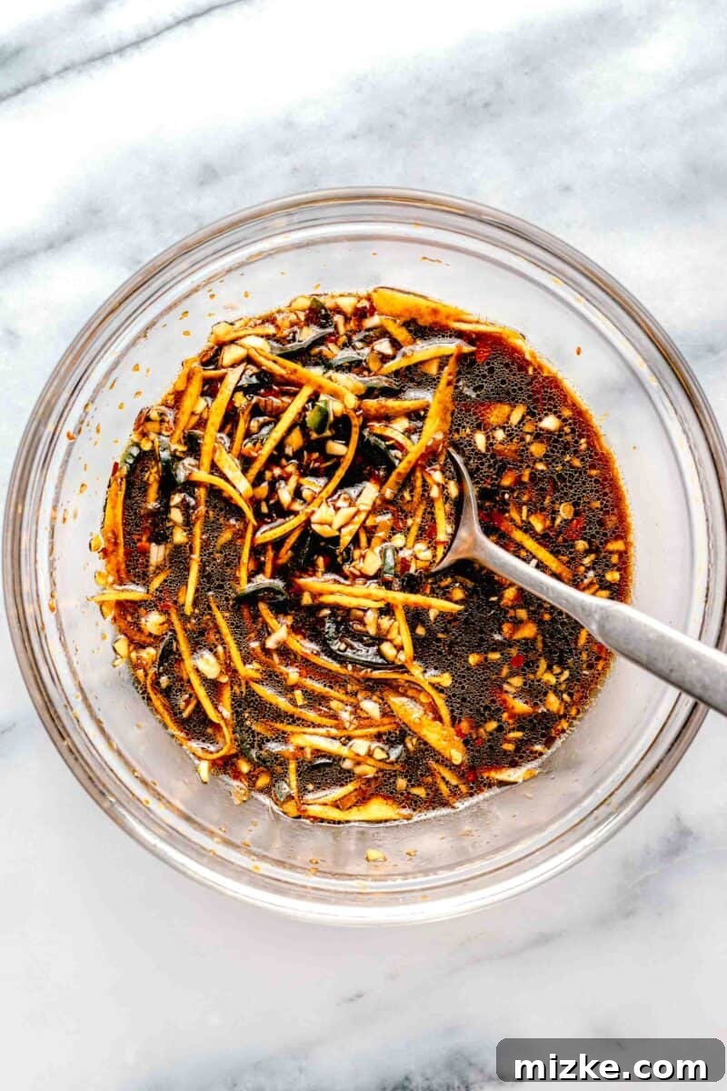 Whisking the sweet, savory, and spicy citrus sauce for crispy beef. A medium bowl containing various sauce ingredients being whisked together, including orange zest, liquid components, and spices.