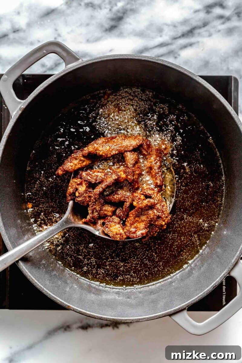 Frying beef to a perfect golden crispness for the crispy beef dish. Thin strips of beef actively frying in hot oil within a deep pot, turning golden brown.
