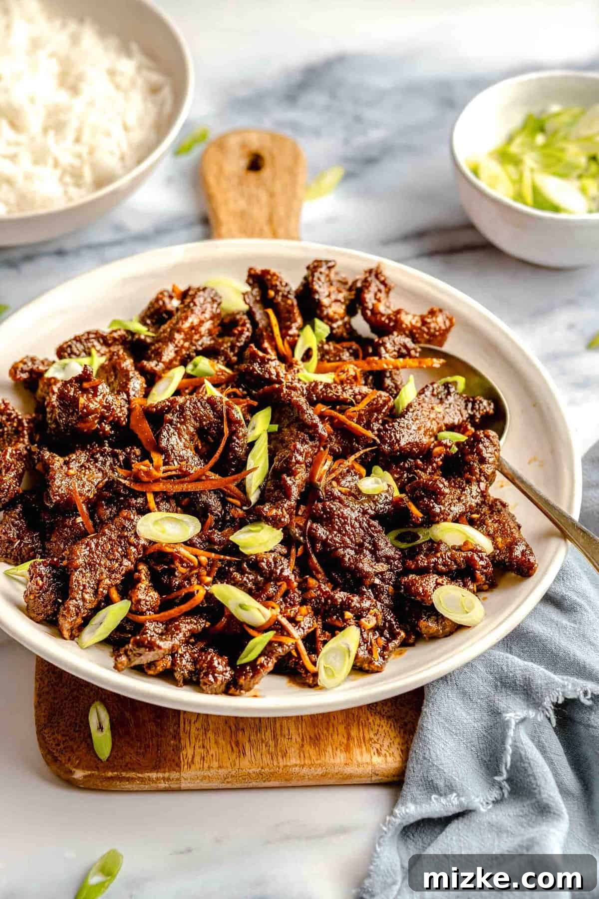 Crispy beef served alongside a bowl of steamed jasmine rice. A serving platter of crispy beef presented on a rustic wooden board, accompanied by a bowl of fluffy white rice.