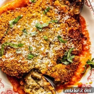 Crispy Fried Eggplant Cutlets 4 A close-up of a breaded and cooked eggplant schnitzel, garnished with fresh basil and grated cheese, on a floral plate, ready to be enjoyed.
