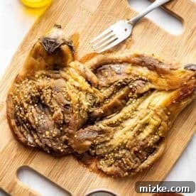 Crispy Fried Eggplant Cutlets 7 A roasted and peeled eggplant being flattened with a fork on a wooden cutting board, with olive oil, salt, and pepper in small bowls around it.