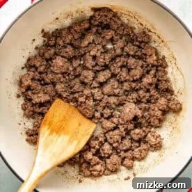Cooked ground beef in a red pot with a wooden spatula, shown from above.