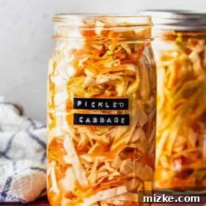 A glass jar filled with vibrant pickled cabbage sits on a pink surface, labeled 'Pickled Cabbage', with another jar and a fork nearby.