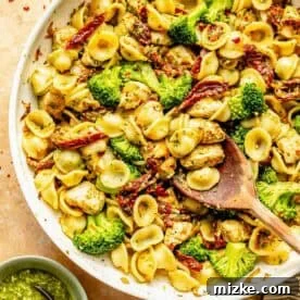 20 Quick Chicken Dinners for Busy Weeknight Meals 2 A skillet filled with orecchiette pasta, broccoli, sun-dried tomatoes, and chicken pieces. A wooden spoon is in the skillet. A small bowl of basil pesto is next to the skillet.