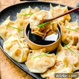 Chopsticks picking up shrimp shumai from a plate with soy sauce.