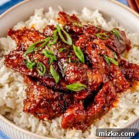 A bowl of white rice topped with Mongolian beef and garnished with chopped green onions.