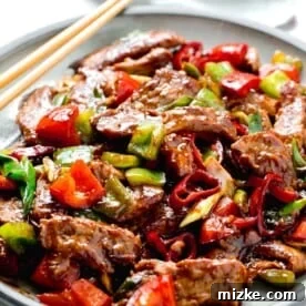 a large plate of hunan beef with wooden chopsticks sitting on the grey ceramic plate next to a light green towel