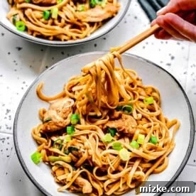 2 bowls of chicken lo mein with chopsticks next to sliced scallions.
