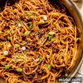 A pan of stir-fried noodles with minced meat, topped with sliced green onions and sesame seeds.