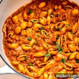 ground beef with pasta shells in a cast iron skillet next to a yellow checkered linen towel with fresh parsley garnished on top