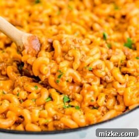 a wooden spoon scoops up cheesy pasta from a cast iron skillet
