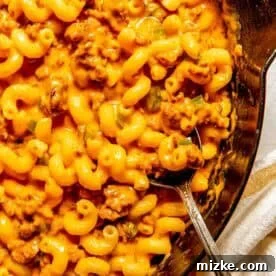 A skillet filled with cheesy macaroni pasta mixed with ground chorizo and a metal spoon resting inside.