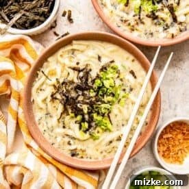 udon noodle soup in a clay bowl topped with seaweed and green onions with wooden chopsticks sitting on the bowl
