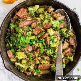 Overhead view of orange beef in a skillet with a metal serving spoon.