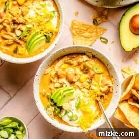 two bowls of southwest chicken chili topped with shredded cheese, avocado slices, sour cream, and tortilla chips