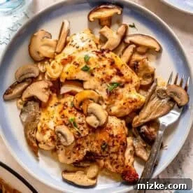Creamy mushroom chicken served with a creamy mushroom sauce and garnished with fresh herbs on a round plate, accompanied by a fork and knife.