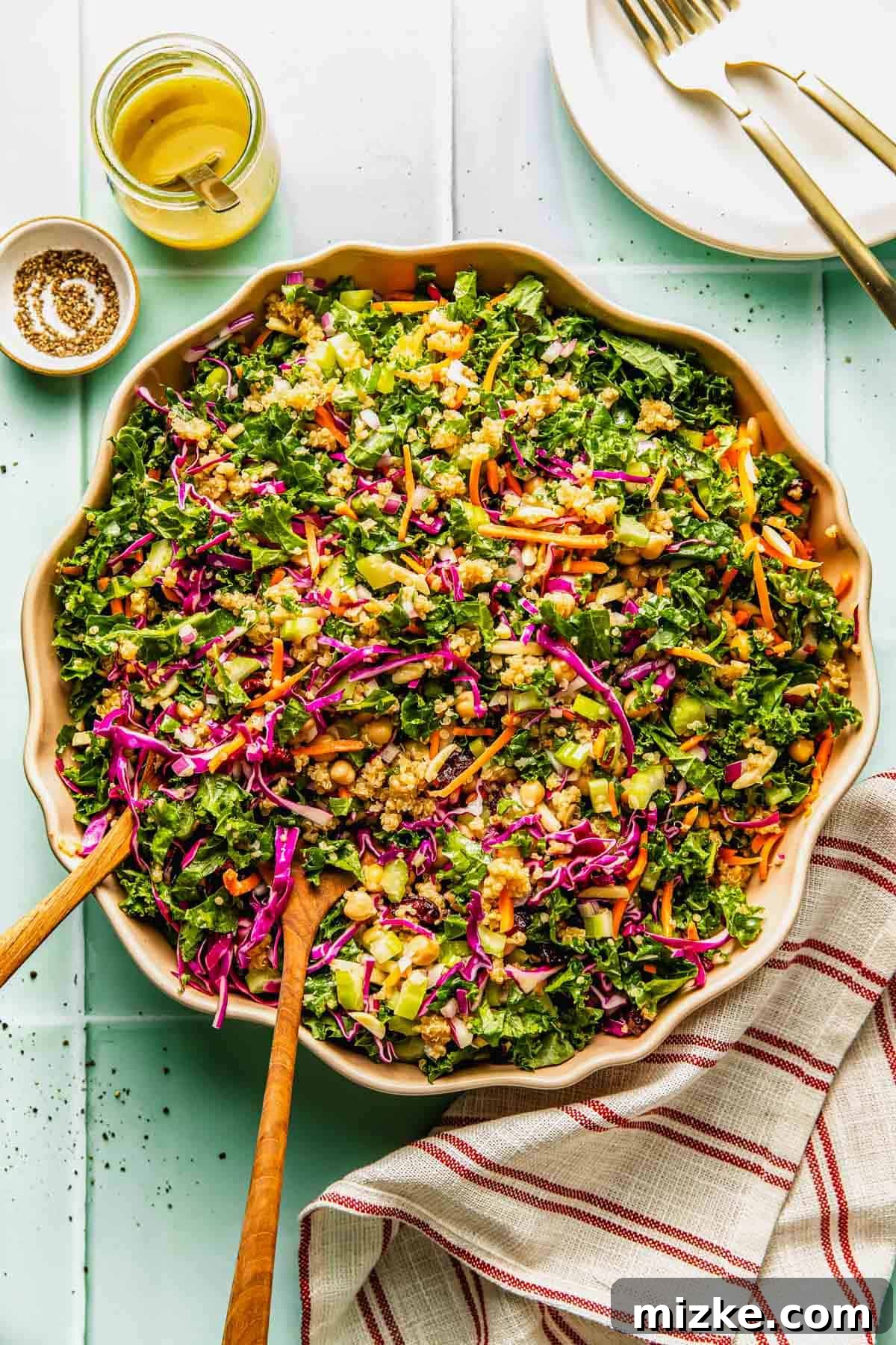 Crunchy Celery and Quinoa Salad with Lemon Vinaigrette 2 Large bowl of chopped kale salad with shredded carrots, red cabbage, green onions, peanuts, and dressing, placed on a light surface with utensils and a striped napkin nearby.