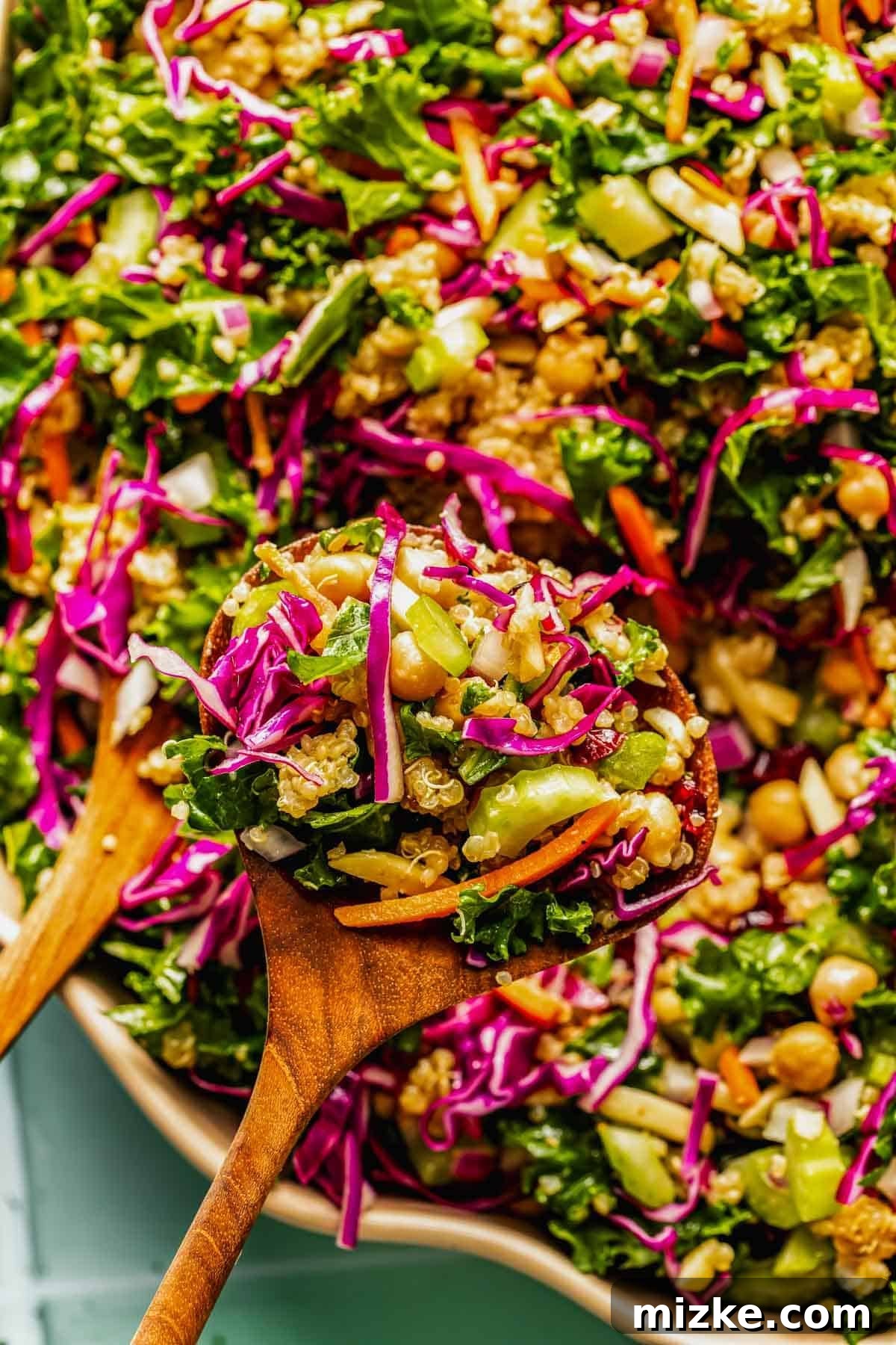 Crunchy Celery and Quinoa Salad with Lemon Vinaigrette 3 A wooden spoon holds a colorful salad with shredded kale, red cabbage, carrots, cucumbers, chickpeas, and quinoa.