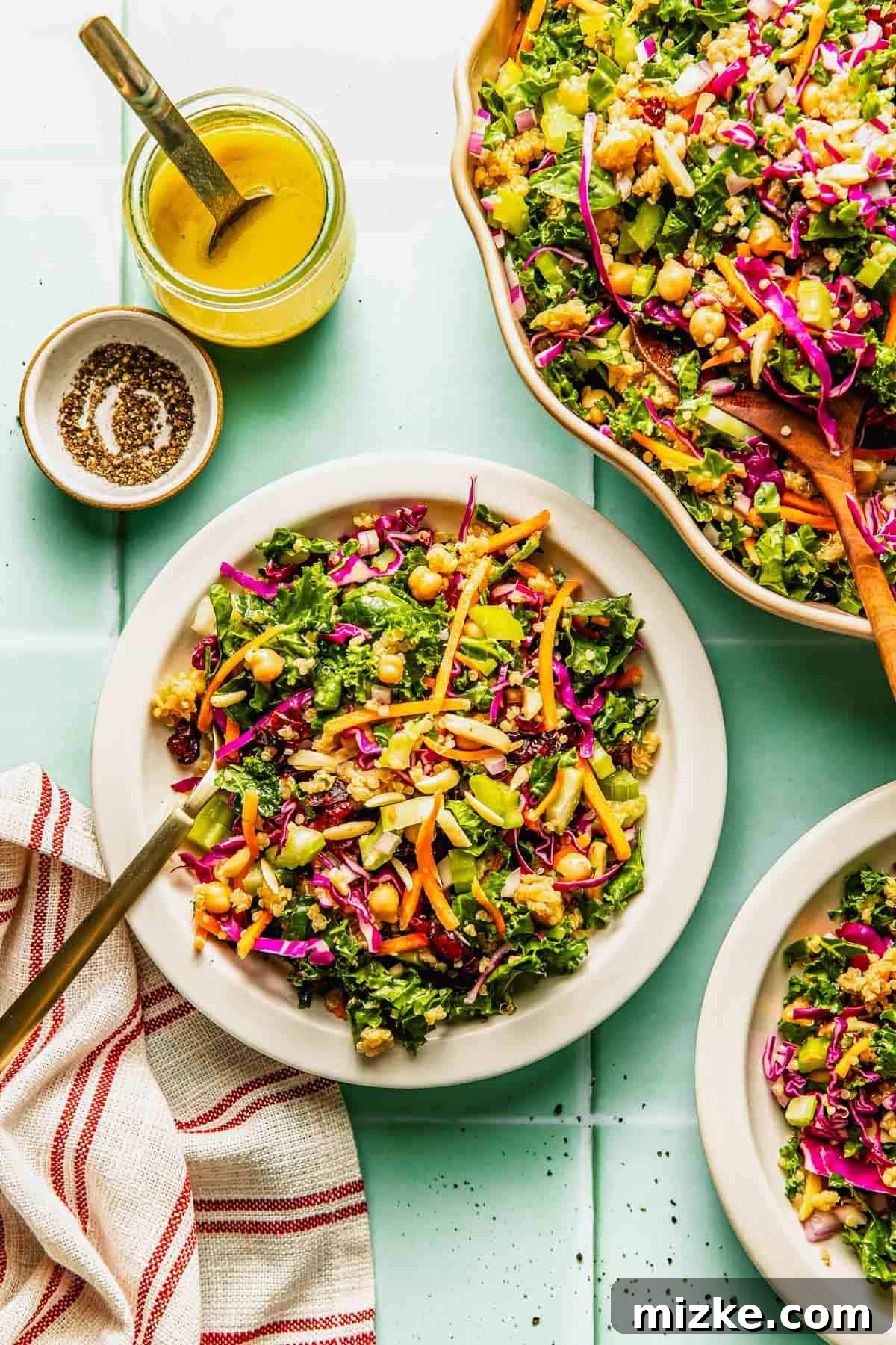 Crunchy Celery and Quinoa Salad with Lemon Vinaigrette 4 A plate of chopped kale salad with colorful vegetables, chickpeas, and a side of yellow dressing, shown on a light blue table with a striped napkin.